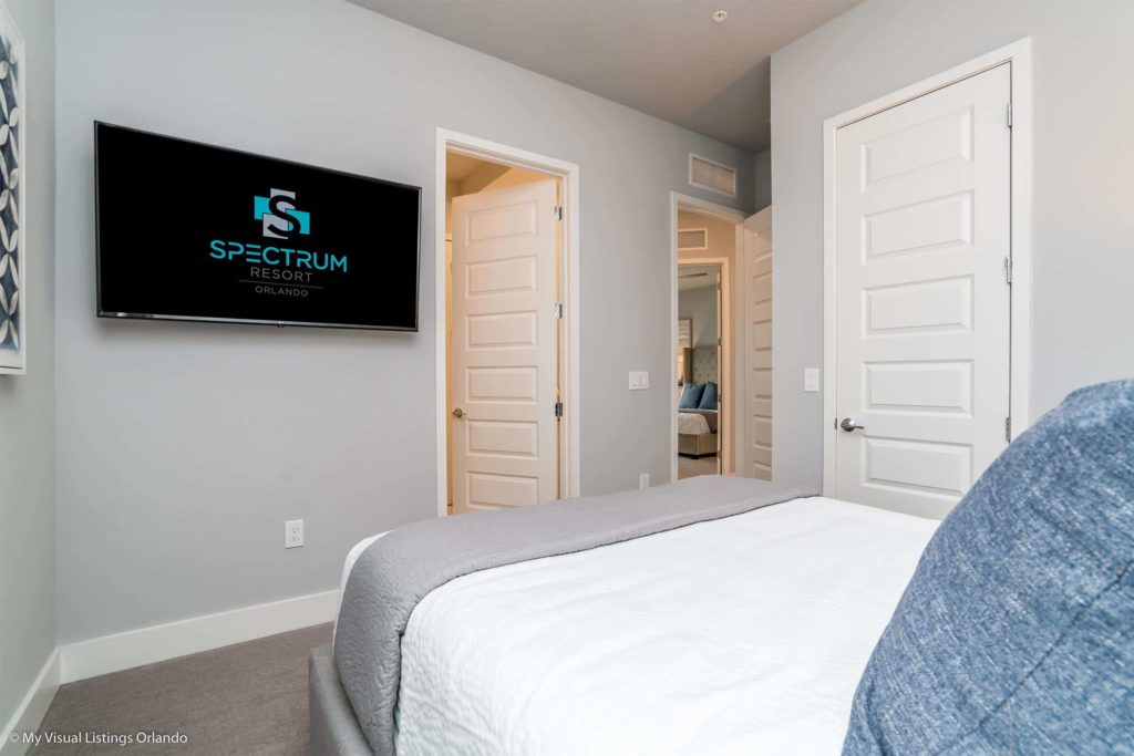 Dormitorio en suite amueblado con TV, grandes puertas de armario y ventana dentro de una casa de vacaciones en alquiler de Spectrum Resort Orlando.