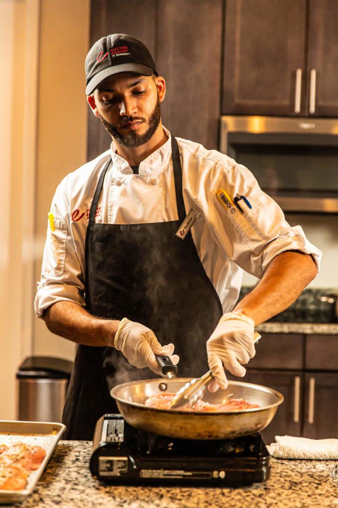 An Encore Resort रीयूनियन विशेषज्ञ शेफ घर में शेफ के अनुभव के दौरान खाना बनाता है।