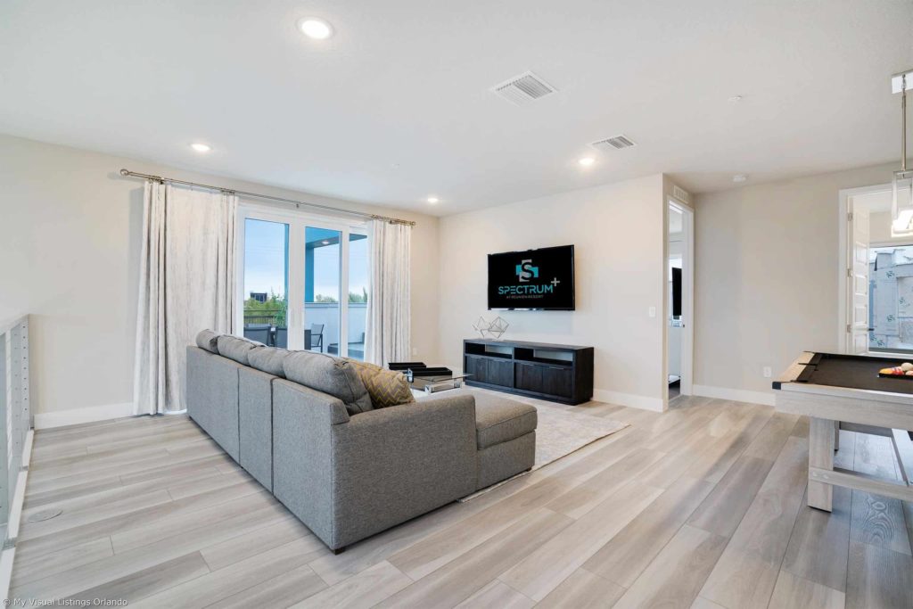 Loft amueblado con sofá, TV, mesa de billar y acceso al balcón dentro de una casa de vacaciones en alquiler de Spectrum Resort Orlando.