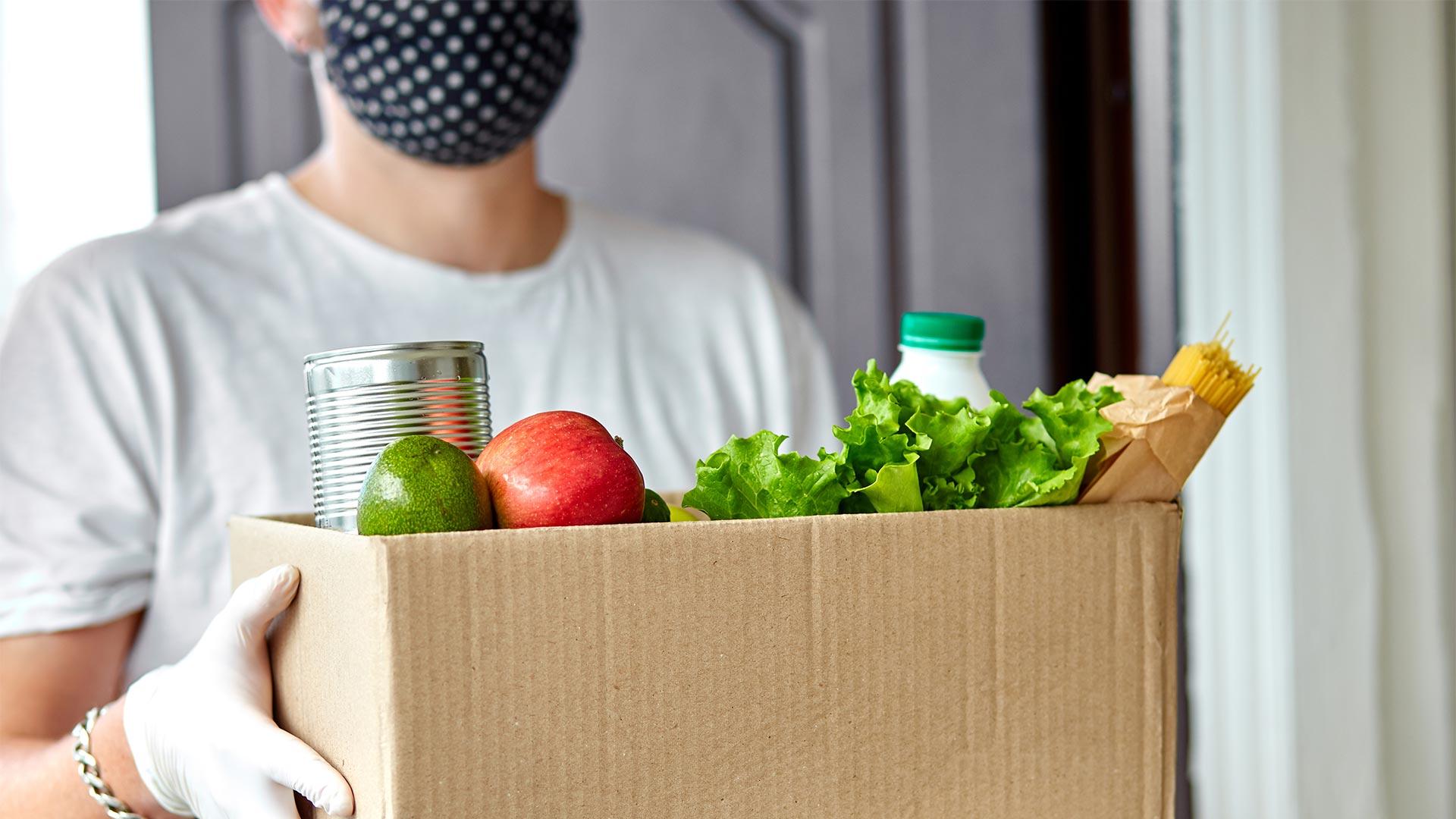 Person carrying a box of groceries while wearing a protective face mask and gloves.