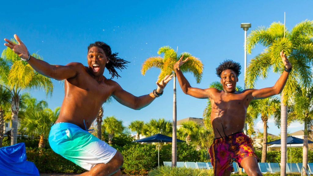 Two young men jumping into the Encore Resort pool as they smile for the camera.