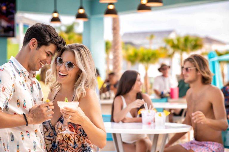 Casal abraçado enquanto brinda com drinks tropicais no Margaritaville Resort Orlando's Salty Rim Bar & Grill.