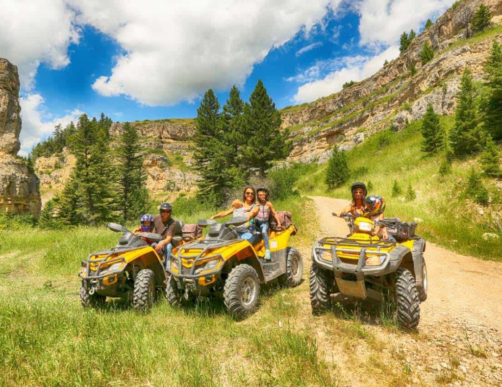 عائلة مع أطفال وأولياء الأمور يركبون مركبات ATV عبر منطقة Big Sky Country في مونتانا في The Ranches at Belt Creek.