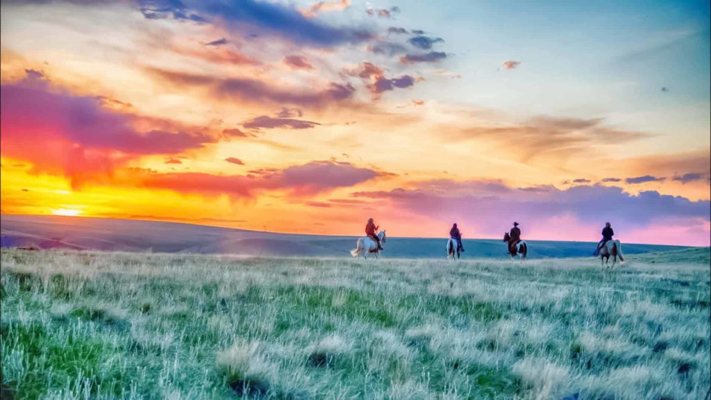 Jinetes a caballo bajo un colorido atardecer en The Ranches at Belt Creek en Montana.