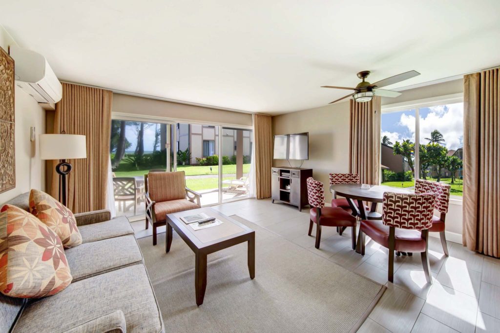 Sala de estar amueblada de una residencia de Pono Kai Resort con sofá, mesa de comedor, mesa de café y puertas corredizas de vidrio.
