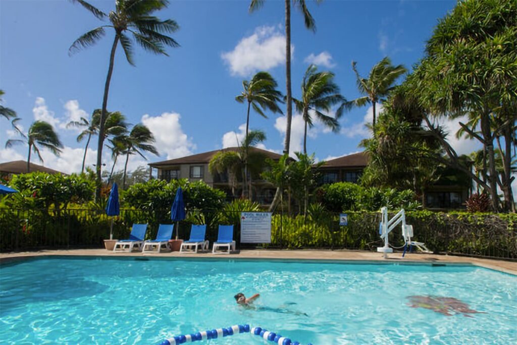 Young boy swimming in the Pono Kai Resort pool surrounded by gardens and palm trees.