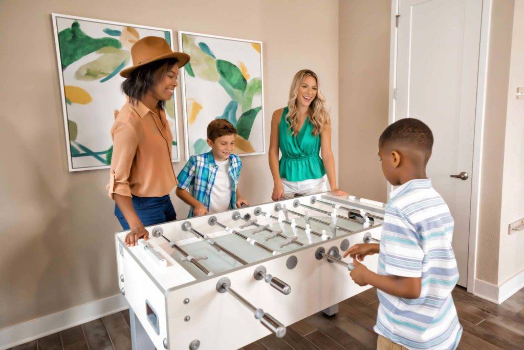 Two kids playing a game of foosball with their moms in the loft of a Spectrum Resort Orlando resort residence.