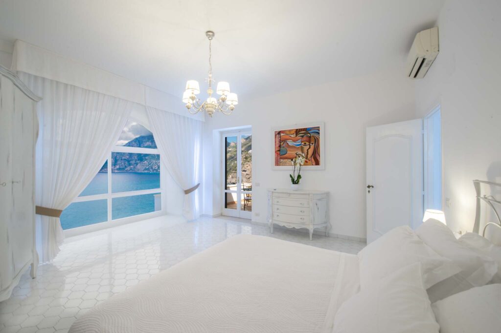 Dormitorio en Villa Lilly con una gran ventana con cortinas que da al mar Tirreno y la costa de Amalfi.