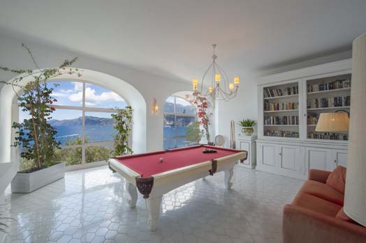 Biblioteca y sala de juegos con mesa de billar en la villa principal de Villa Lilly con grandes ventanales que ofrecen impresionantes vistas del mar Tirreno y la costa de Amalfi.