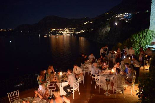Private event with banquet tables set up on Villa Lilly’s outdoor balcony overlooking the Tyrrhenian Sea at night.