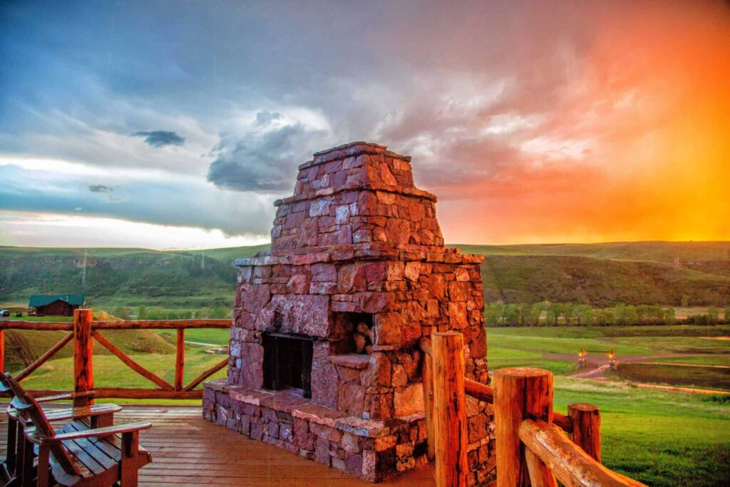Ranches at Belt Creek clubhouse deck with stone fireplace with a colorful sunset backdrop.