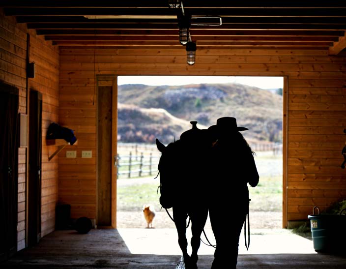 Woman leading a horse into the Ranches at Belt Creek equestrian facility barn.