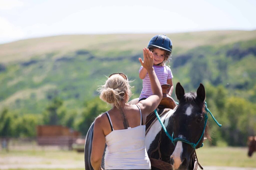 Young girl on horseback high-fives a riding instructor at The Ranches at Belt Creek.