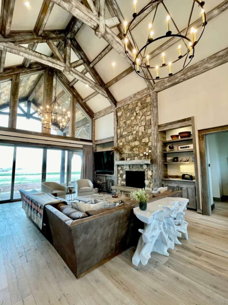Sala de estar rústica de Lucky Man Ranch con grandes ventanas de vidrio y chimenea de piedra