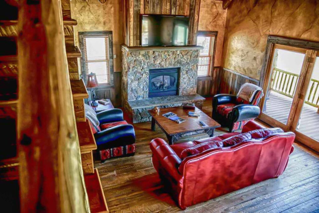 Sala de estar rústica con chimenea de piedra en las cabañas para miembros de The Ranches at Belt Creek.