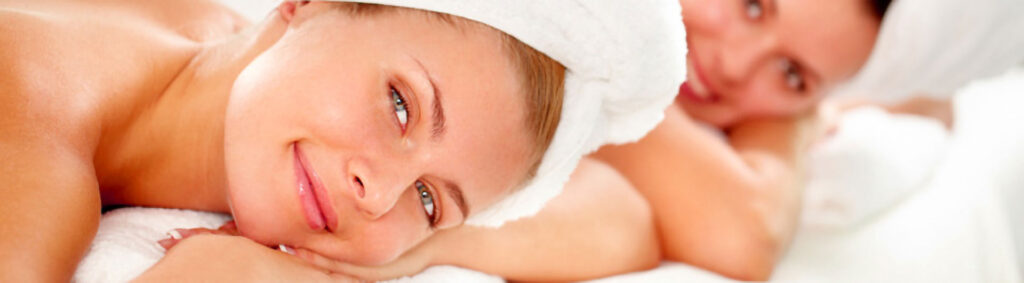 Women lying on spa beds with towels over their hair smiling.