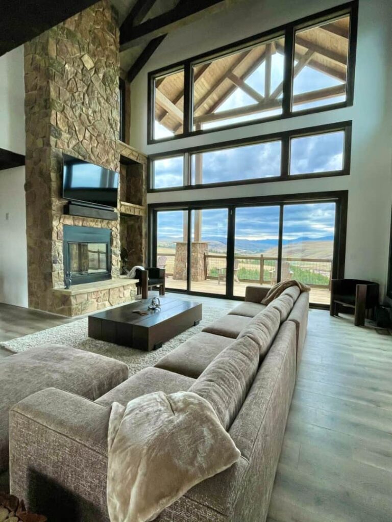 Sunset Ranch spacious living room with stone fireplace and large glass windows offering mountain views