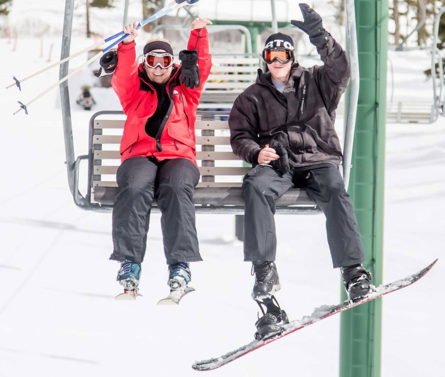 Skier and snowboarder riding a chair lift up a snowy mountain at The Ranches at Belt Creek.