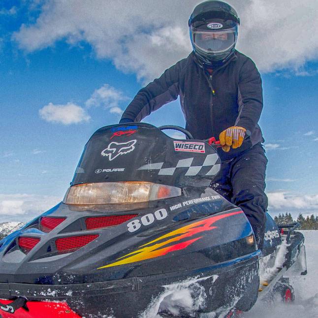 Winter activities with a person riding a snowmobile on The Ranches at Belt Creek’s snow-covered countryside.