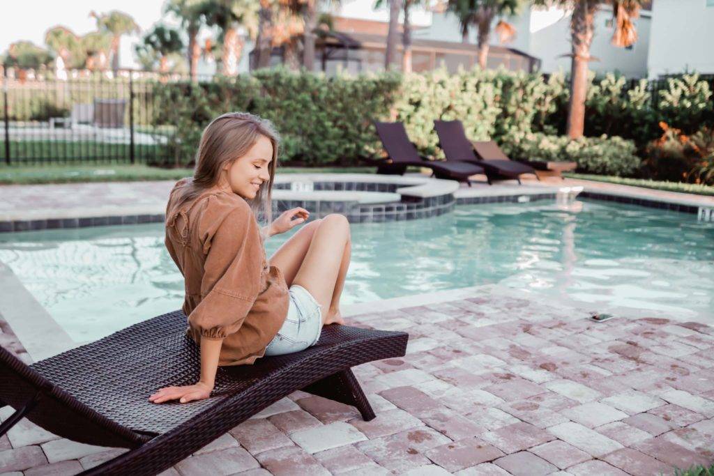 Woman in a light fall jacket relaxing in a lounge chair at her resort residence’s private pool.