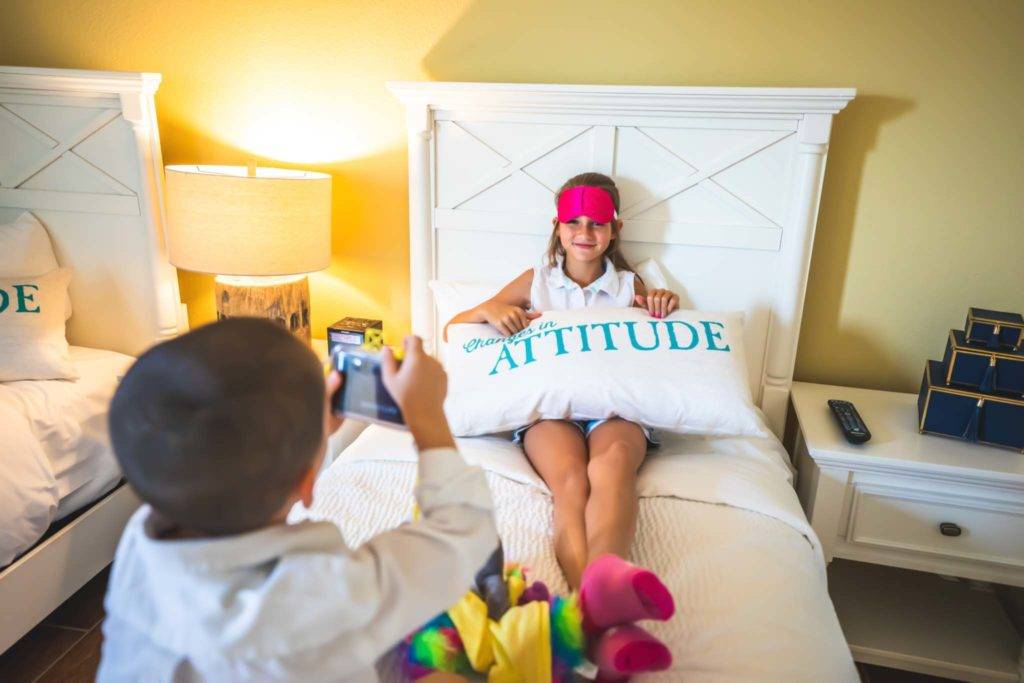 Junges Mädchen, das ein Wurfkissen des Margaritaville Resort Orlando hält, während es auf einem Bett sitzt.