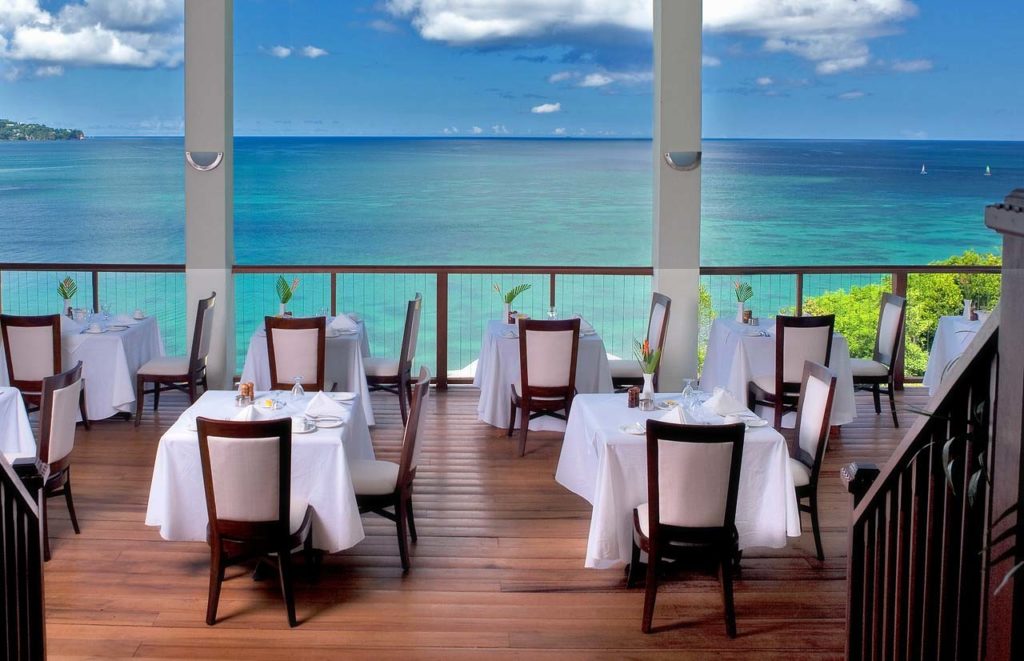 Mesas en el restaurante Windsong de Calabash Cove con vista al cristalino Mar Caribe.