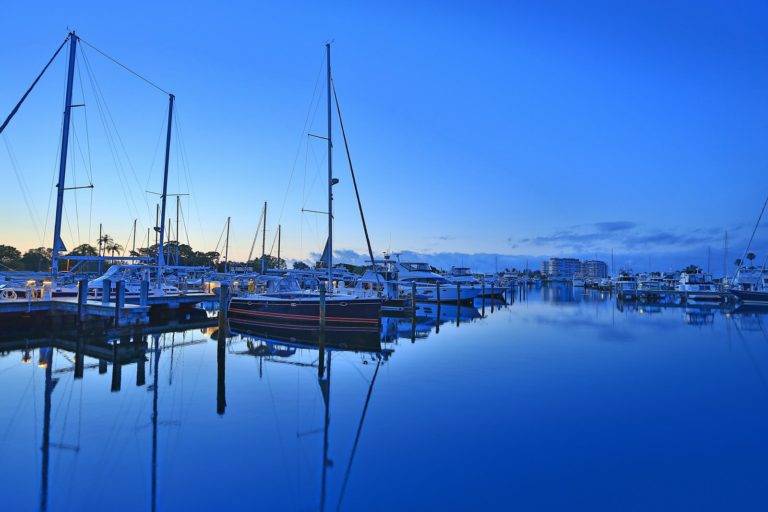 Sailboats in marina at sunrise with other boats and resort in background.