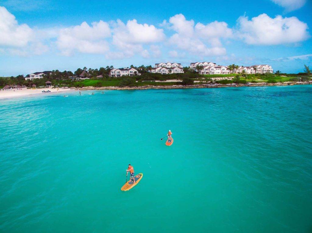 Dos personas practican paddle surf sobre aguas cristalinas frente a la costa de Grand Isle Resort.