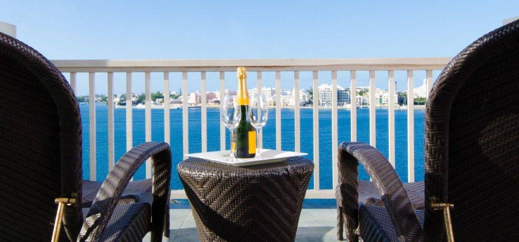 Botella de champán y copas en un balcón privado con vistas al puerto de Hamilton en Rentyl Resorts.