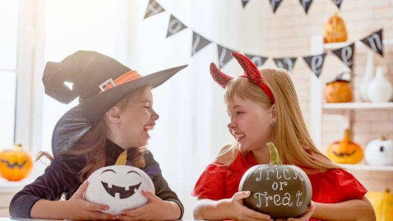 Two Girls In Halloween Costumes Painting Pumpkins.