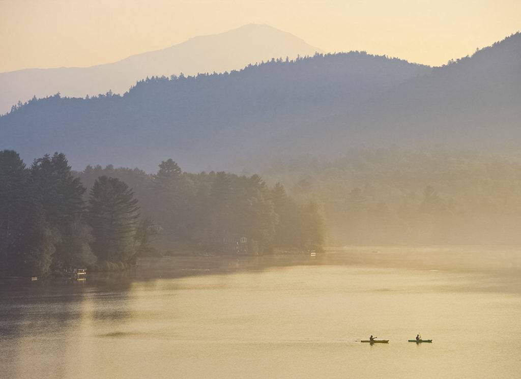Two people canoeing on Mirror Lake amid early morning fog.