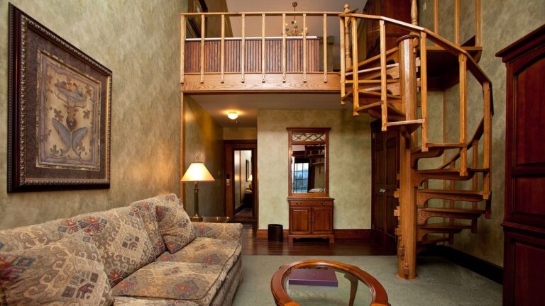 غرفة معيشة في الجناح الكلاسيكي مع أريكة ودرج حلزوني يؤدي إلى دور علوي بسرير كينج