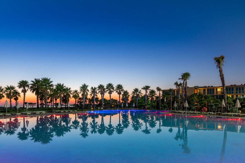 Salgados Dunas exterior pool surrounded by palm trees at sunset.