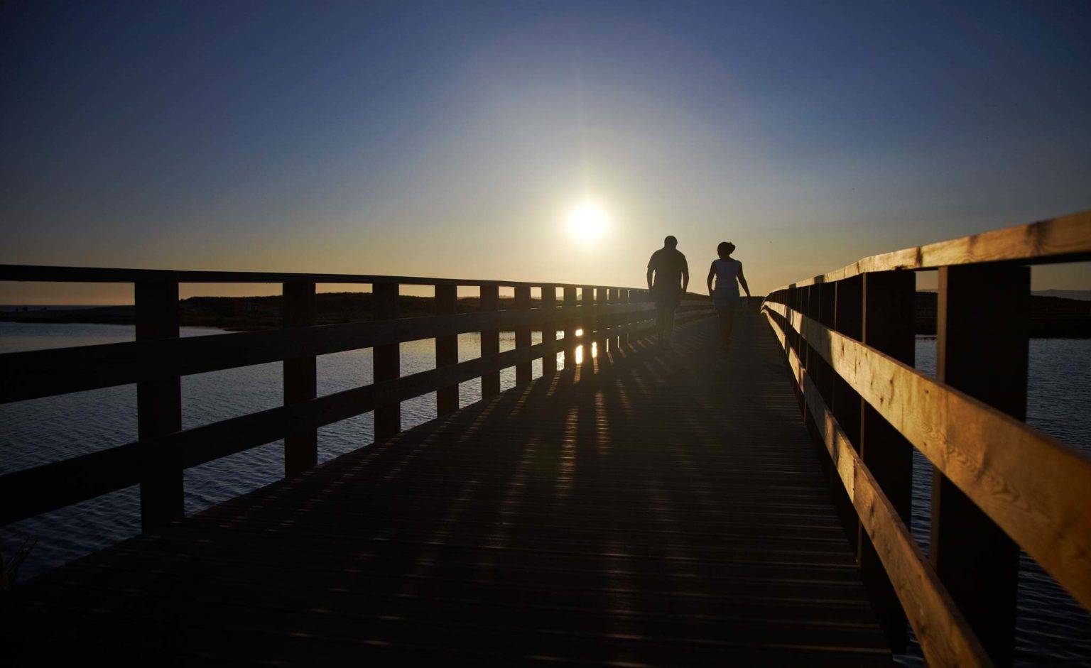 Two people walking on a boardwalk near Salgados Dunas to the beach.