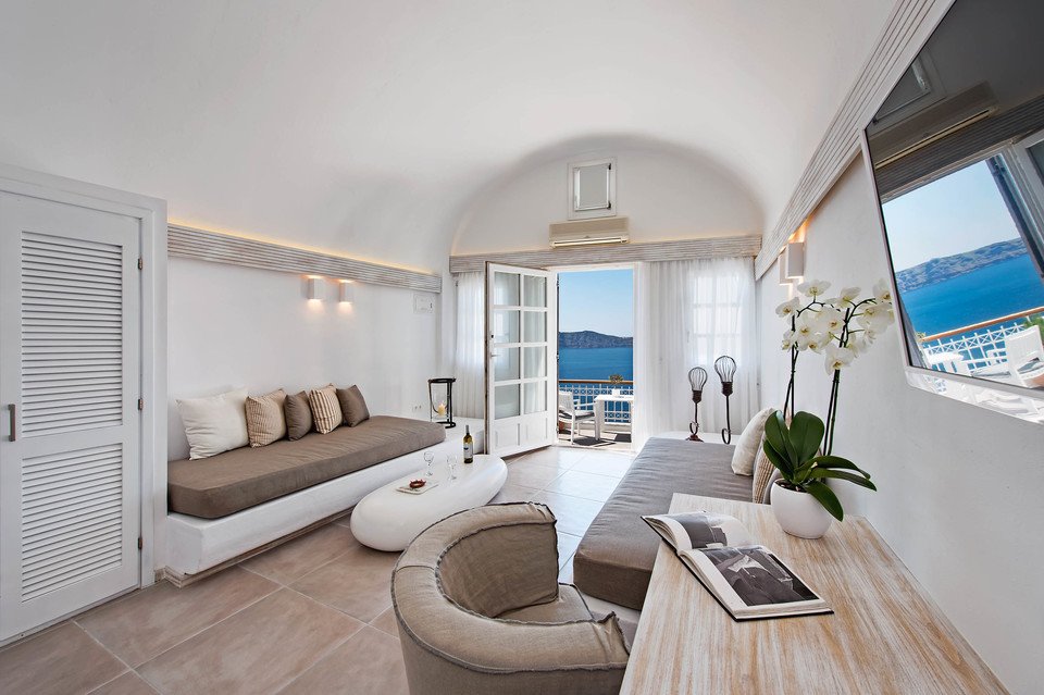 Sala de estar con escritorio, sofás y acceso al balcón con vista al mar en Athina Luxury Suites.