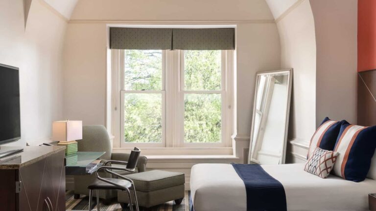 Dormitorio en suite con escritorio, sillón, espejo grande y ventana en The Mansion on Delaware Avenue.