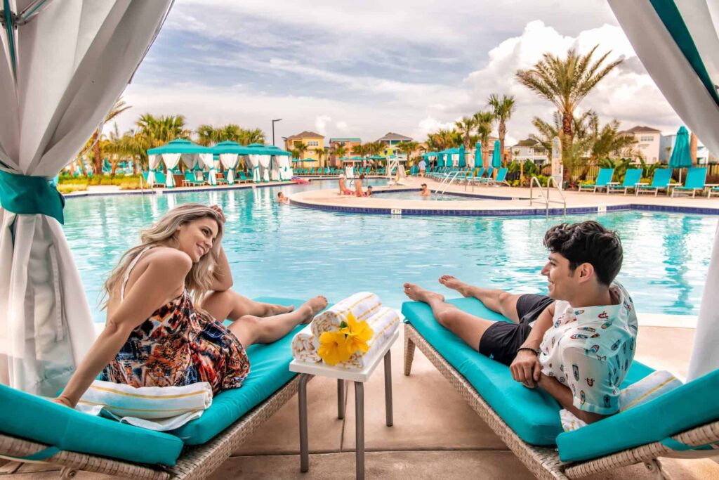 Pareja joven sentados juntos bajo una cabaña privada junto a la piscina del Margaritaville Resort Orlando