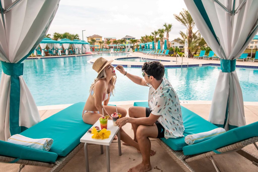 Romantisches Paar teilt Drinks unter einer privaten Cabana am Pool eines Resorts.