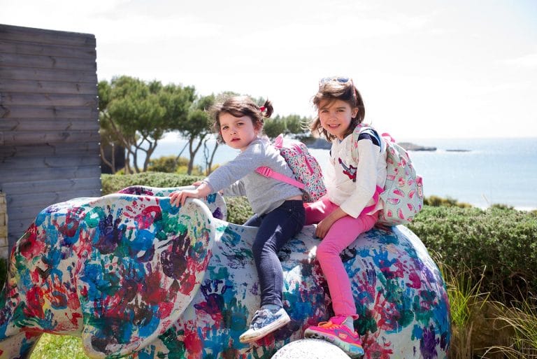 Little girls sitting on an elephant statue covered in handprints