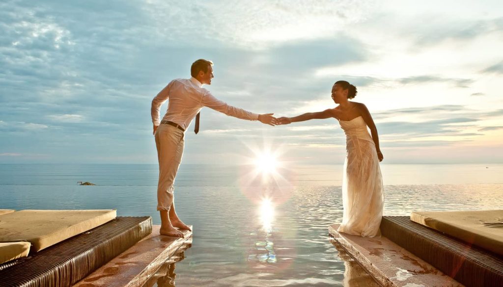 Bride and groom holding hands over the infinity pool at Paresa Resort