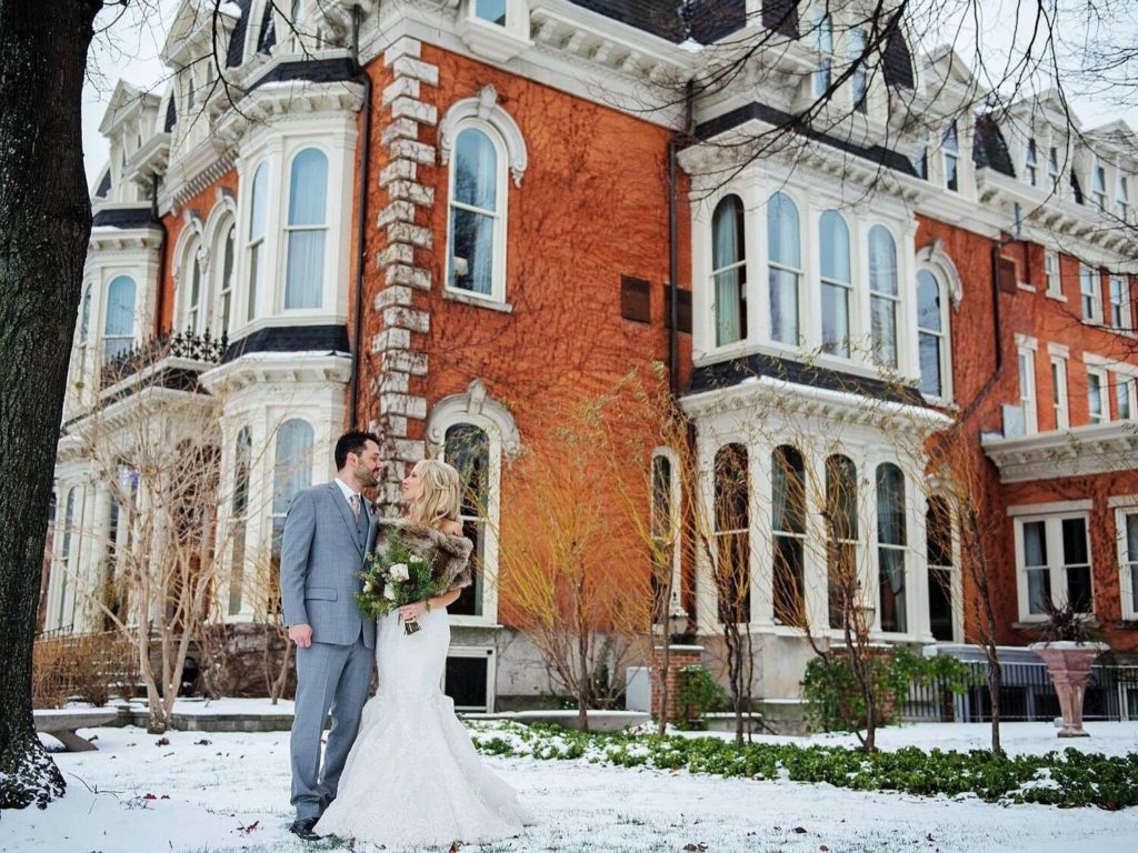 La novia y el novio posando frente a la mansión en Delaware en la nieve.