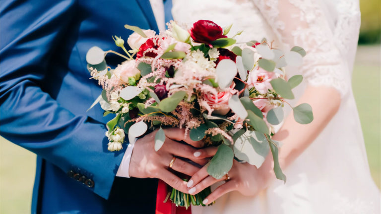 Las manos de la novia y el novio sosteniendo un ramo de novia.