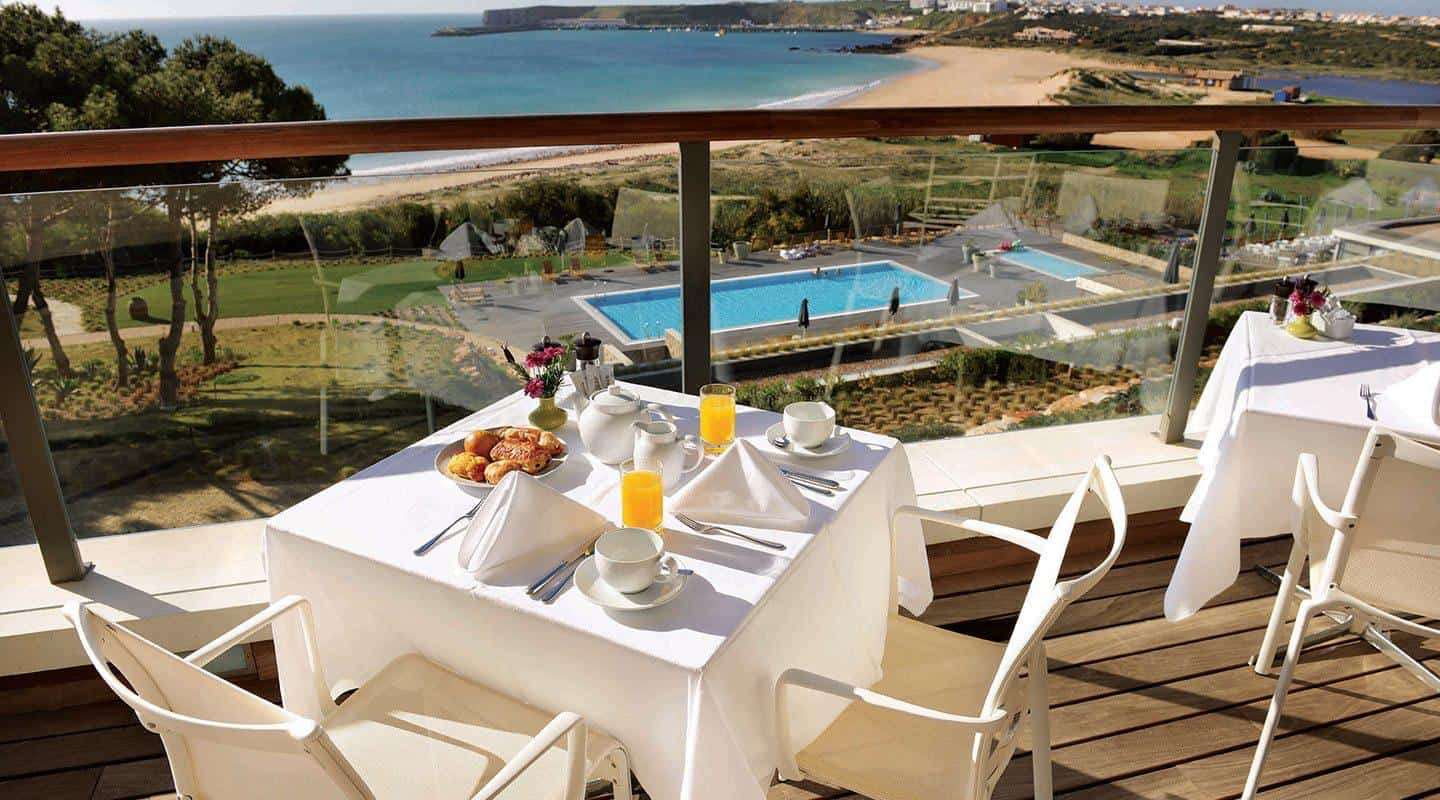 Table set with breakfast on a balcony overlooking a pool and beach
