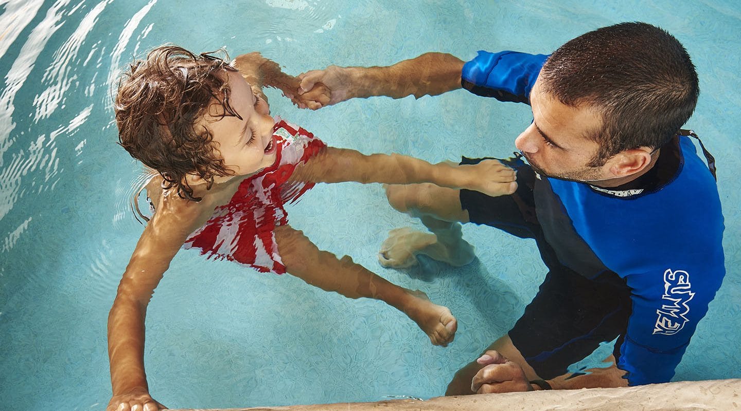 Little boy in a pool with a swim instructor