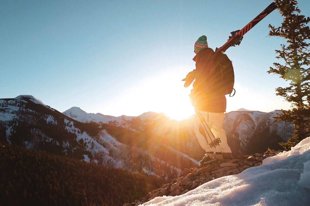 स्कीयर एक पहाड़ की चोटी से सूर्यास्त देख रहा है