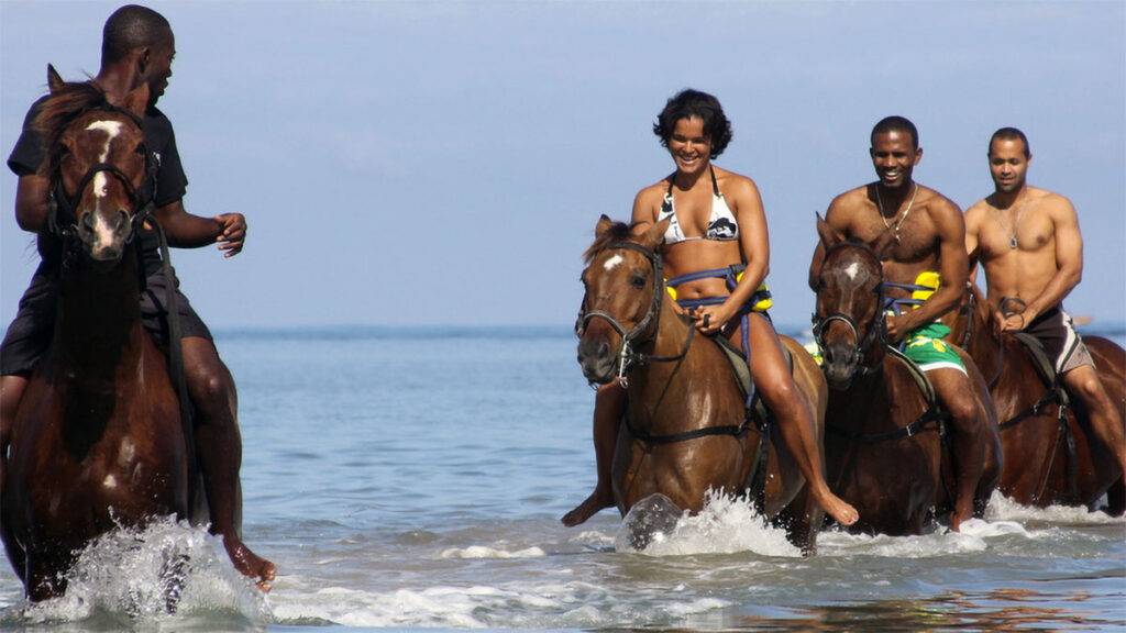 Group of people horseback riding in the shallow waters of the Caribbean Sea.