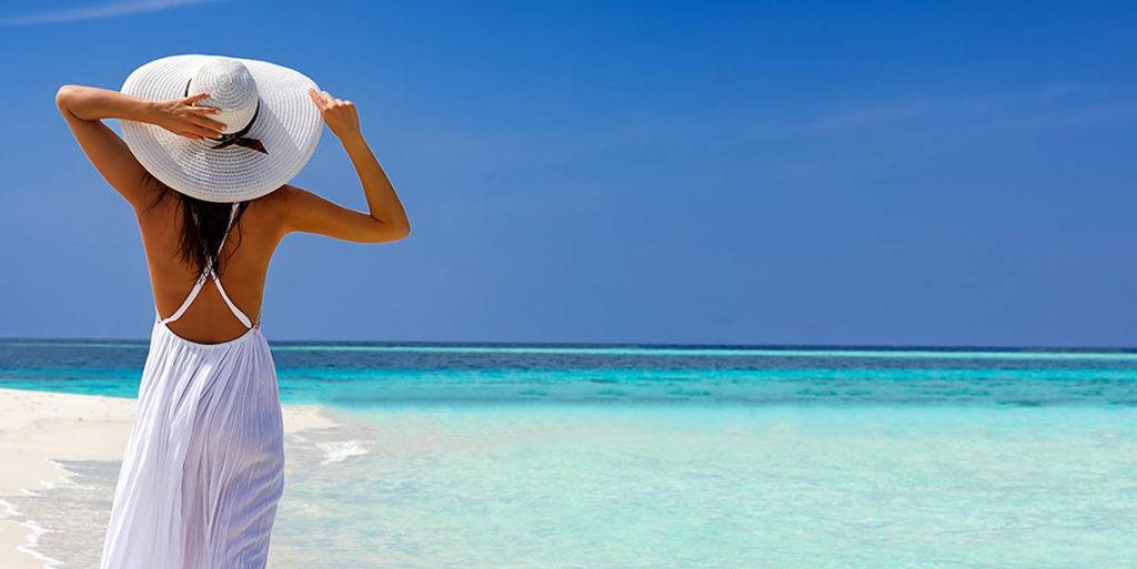 Woman in a sun hat basking on the Caribbean beach.