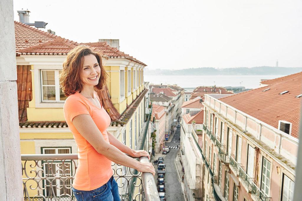 Frau steht auf einem Balkon mit Blick auf Lissabon, Portugal