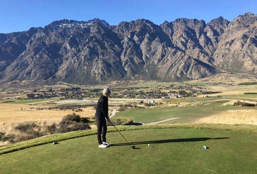 Golfer teeing off with mountain view in the background