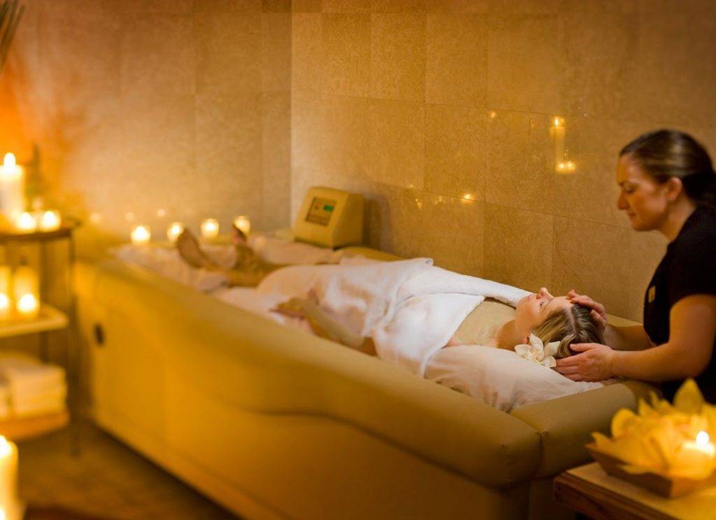 امرأة ترقد على سرير تدليك تحيط بها الشموع في منتجع Mirror Lake Inn الصحي